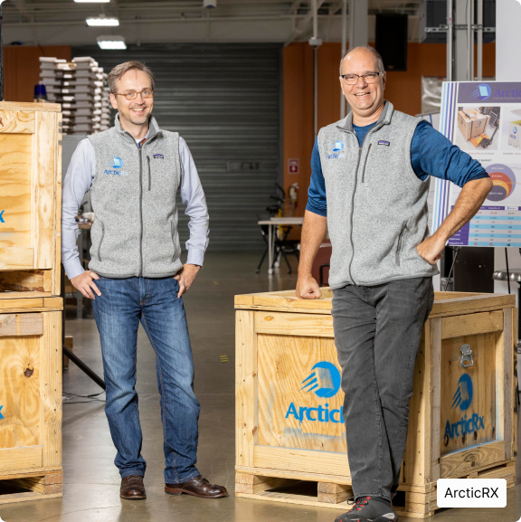 ARTICRX – TWO MEN STANDING BY SHIPPING CONTAINERS, SMILING AT CAMERA
